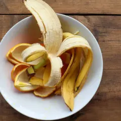 Skórki banana i pomarańczy w białej misce, gotowe na nawóz z banana dla roślin.