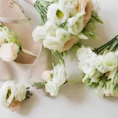Eleganckie, nowoczesne bukiety ślubne i butonierki w pastelowych kolorach, ułożone obok jasnoróżowych butów ślubnych.