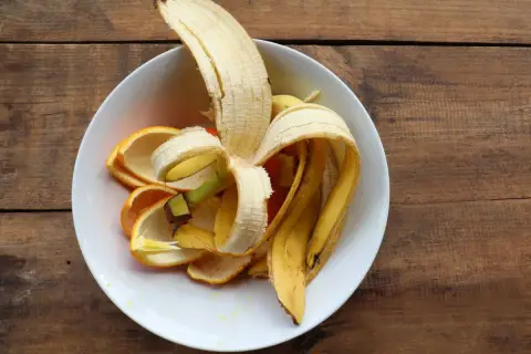 Skórki banana i pomarańczy w białej misce, gotowe na nawóz z banana dla roślin.