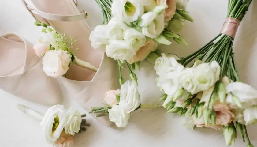 Eleganckie, nowoczesne bukiety ślubne i butonierki w pastelowych kolorach, ułożone obok jasnoróżowych butów ślubnych.